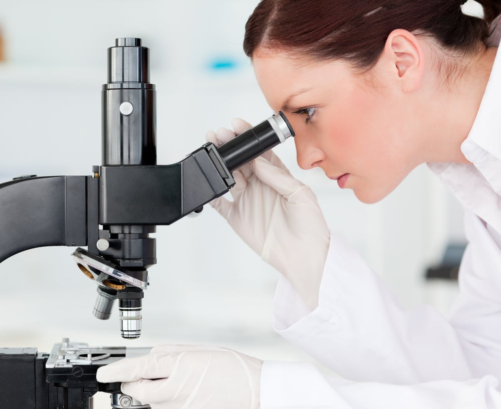 Attractive red-haired scientist looking through a microscope in a lab