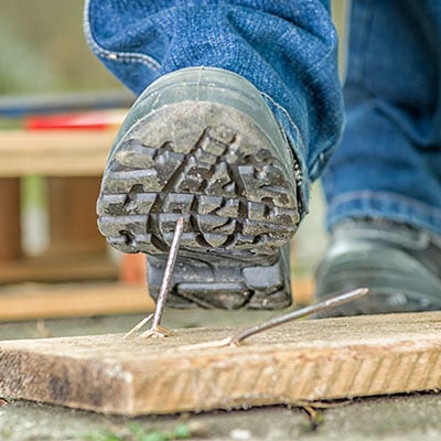 Employee about to suffer a workplace accident by standing on a nail. Is your business taking accident prevention seriously.