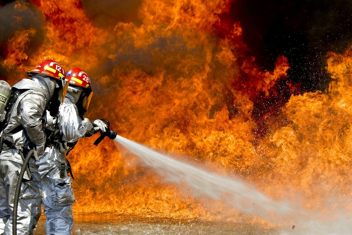 Two people in firefighter suits spraying firefighting foam on fire