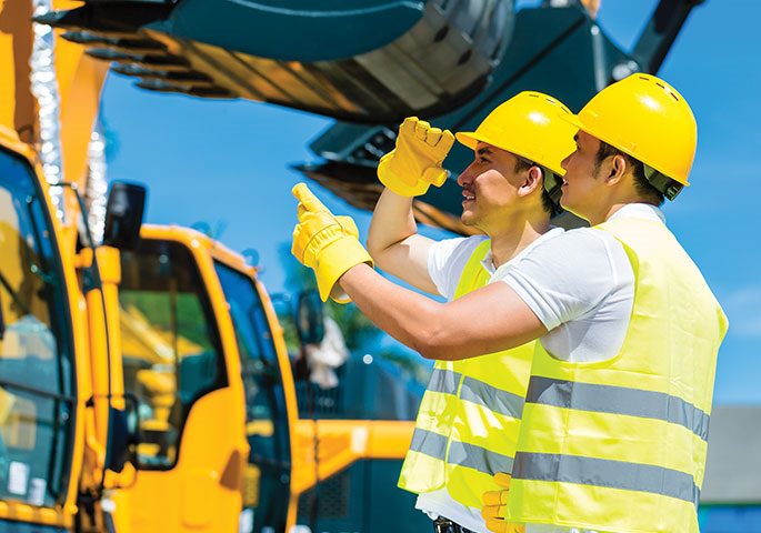 Two men in yellow construction hats pointing to something in the distance in front of a yellow truck
