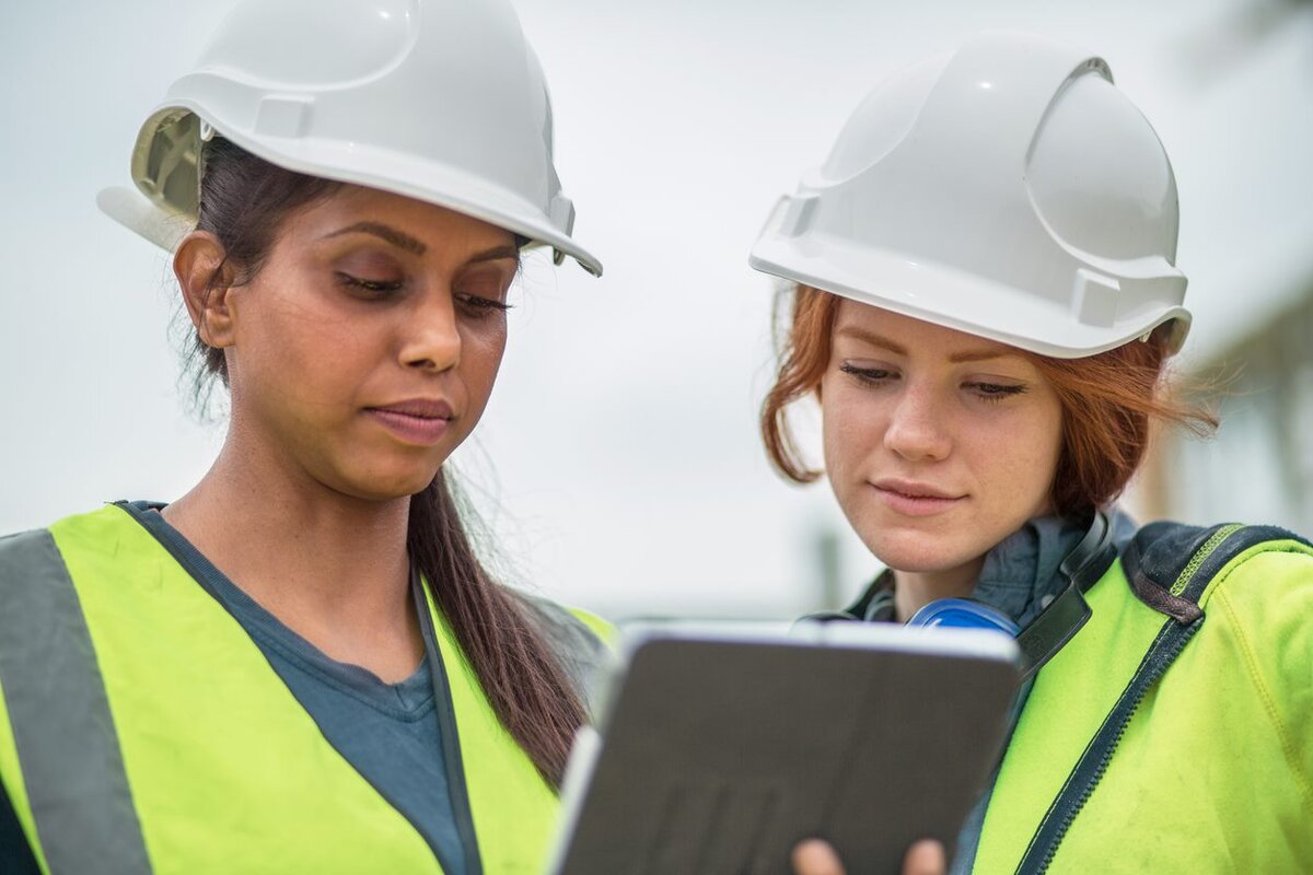 two workers wearing construction hats looking at an ipad