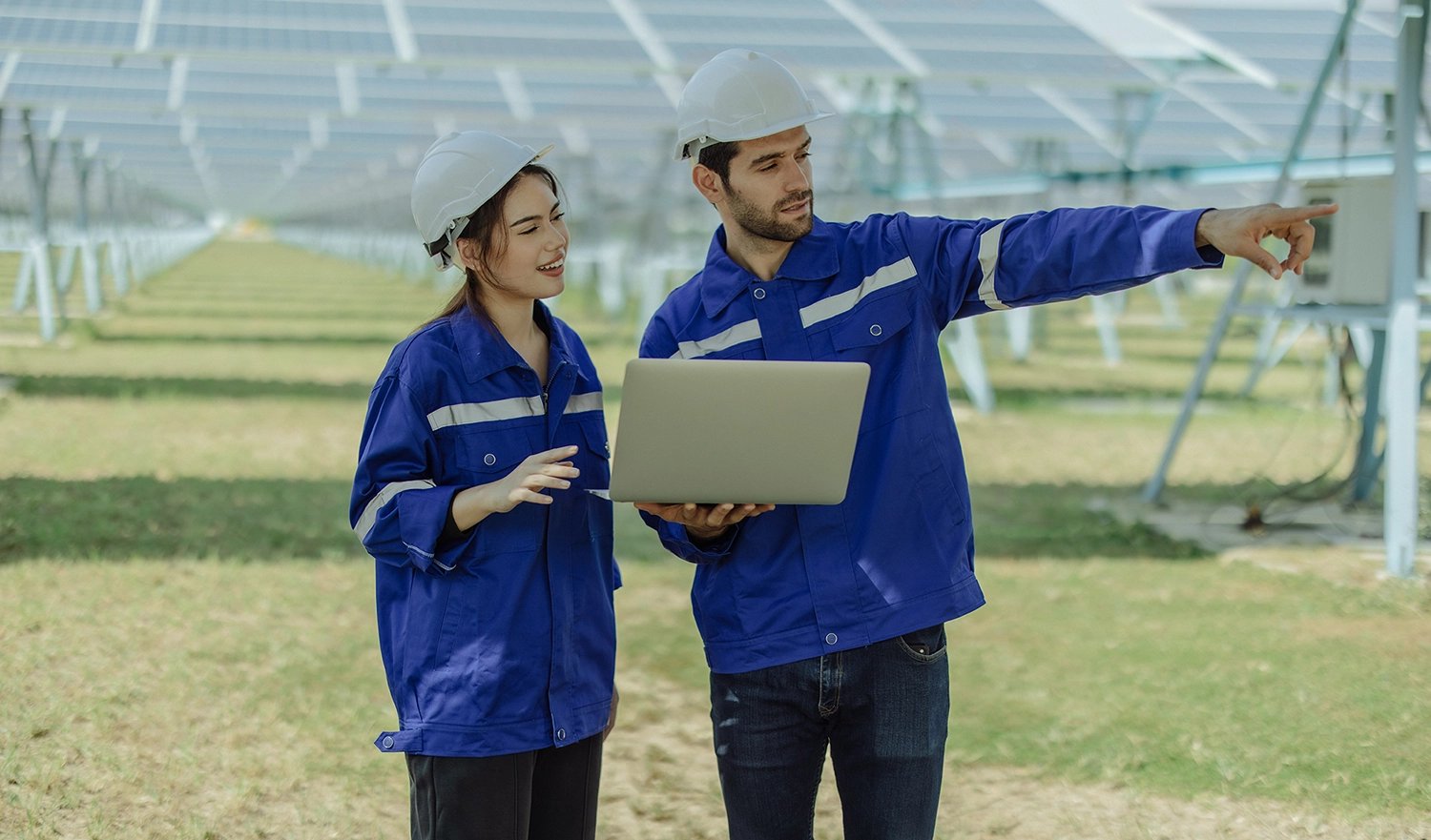 Two people with white heard hats standing with a laptop by solar panels