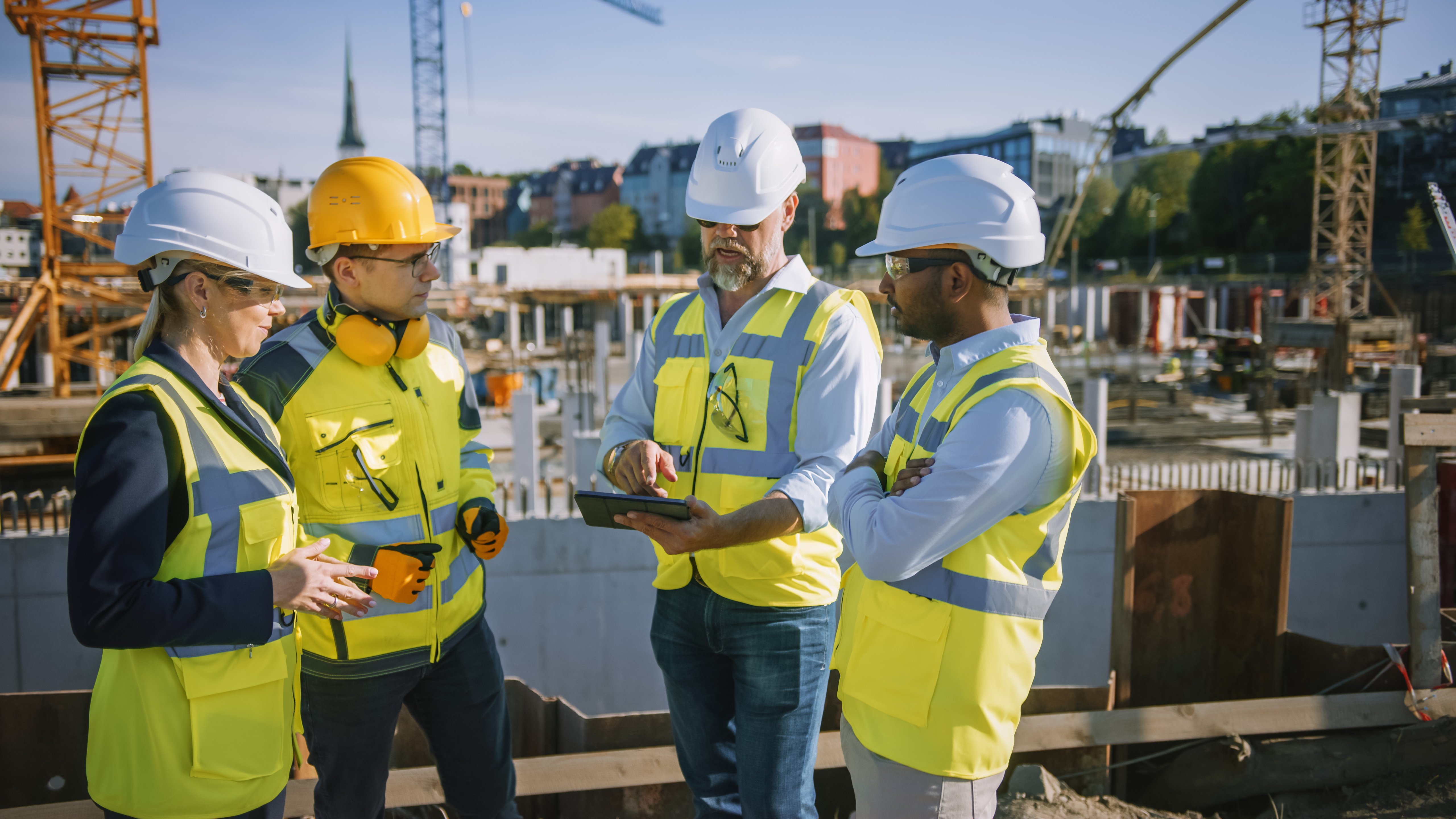 Four people on a construction site with one holding an iPad