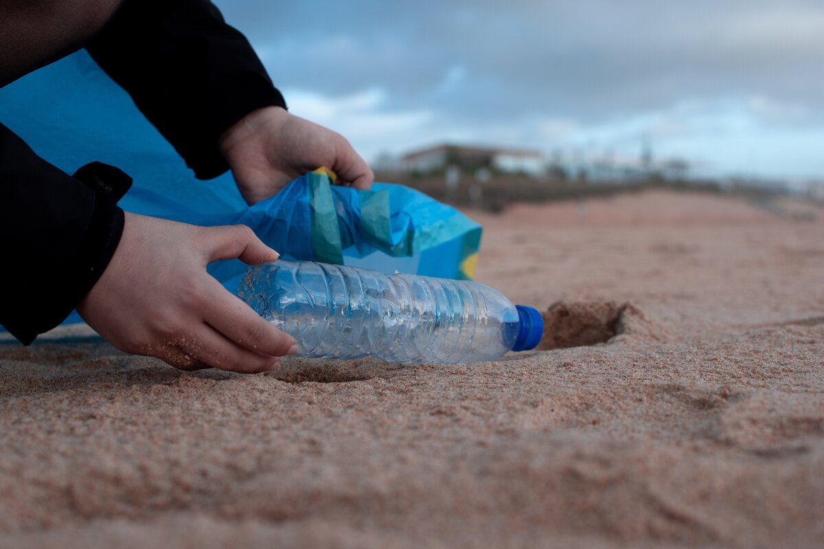 person picking up a bottle from the sand