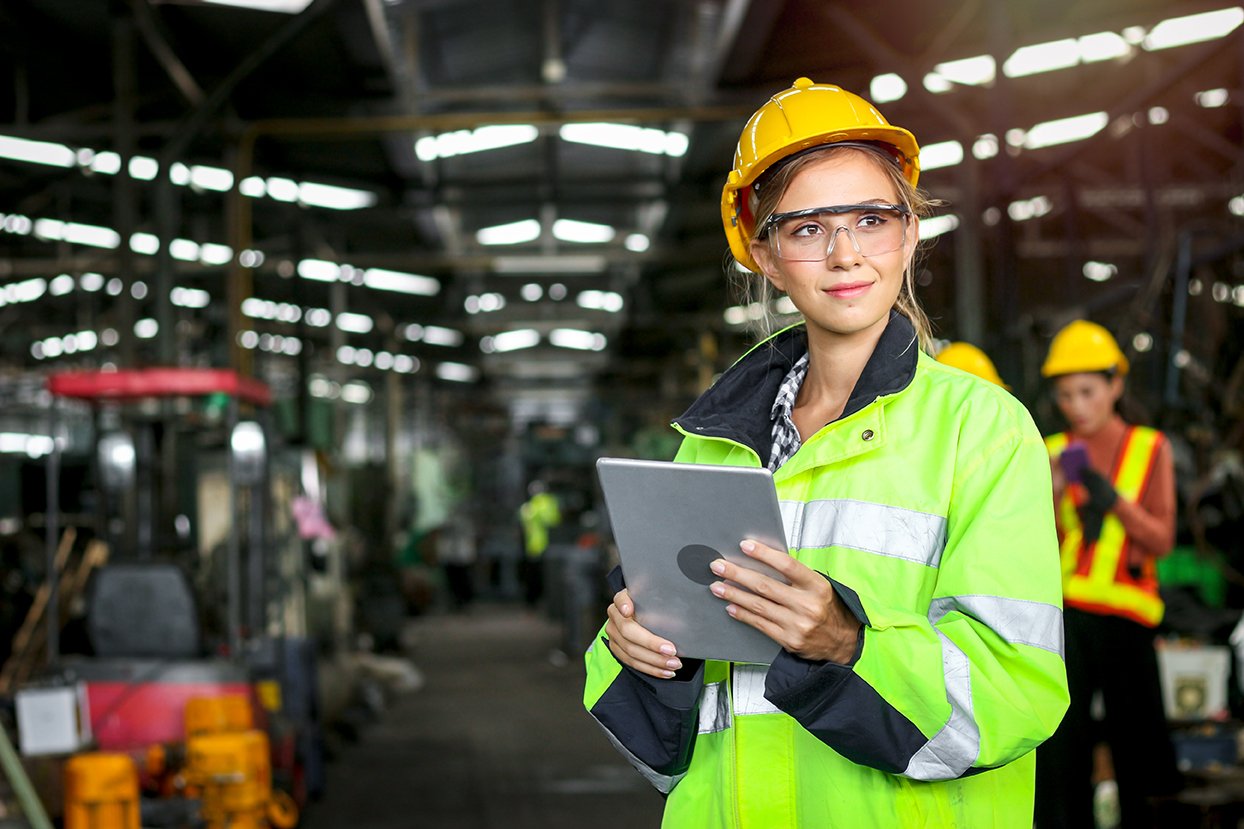 woman wearing safety goals and yellow construction hat holding an iPad in a warehouse