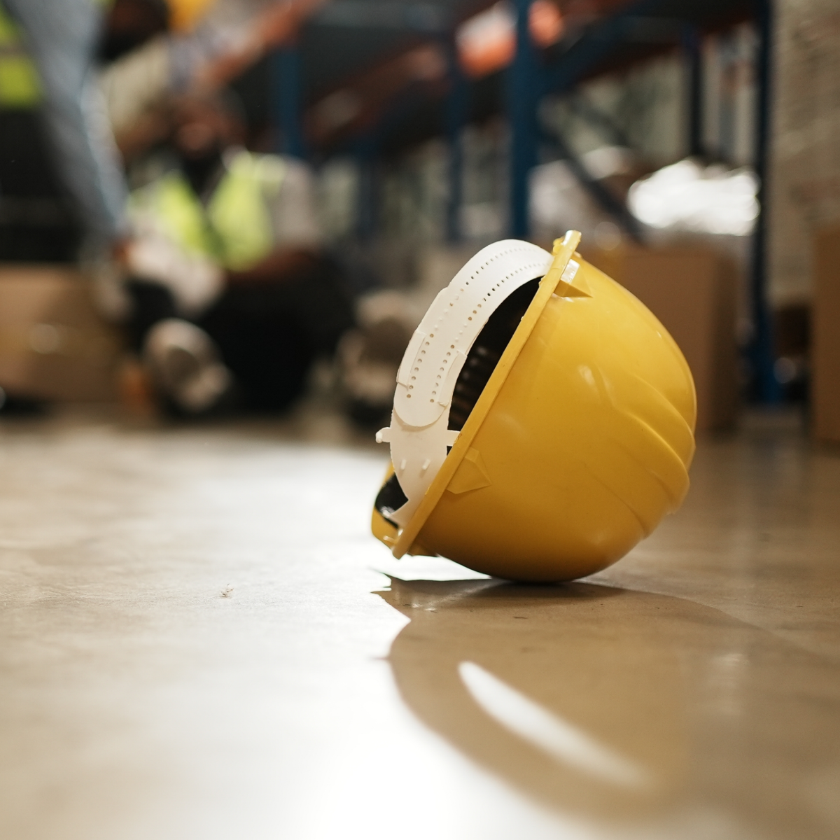 Image of a hard hat discarded on the floor with a workplace accident in the background
